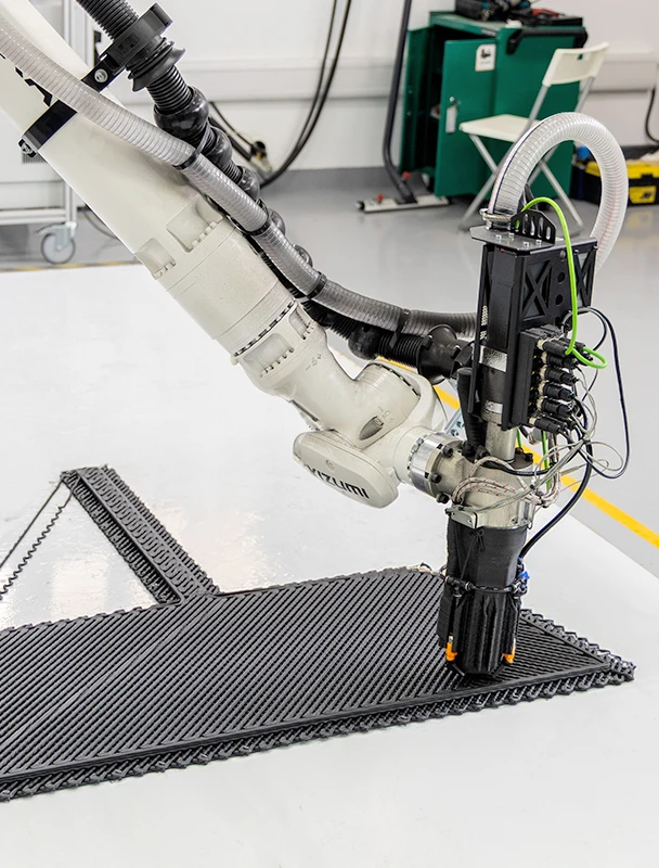A robotic arm begins the 3D printing process, precisely laying down PPCF material using Extrusion Deposition Modeling.